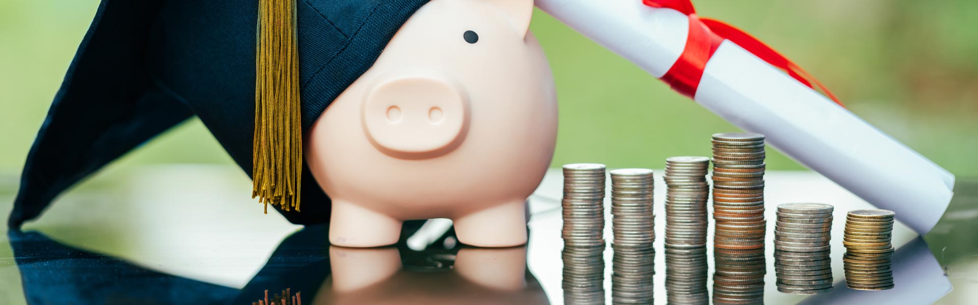 Piggy bank, graduation hat, diploma scroll, and stacks of coins